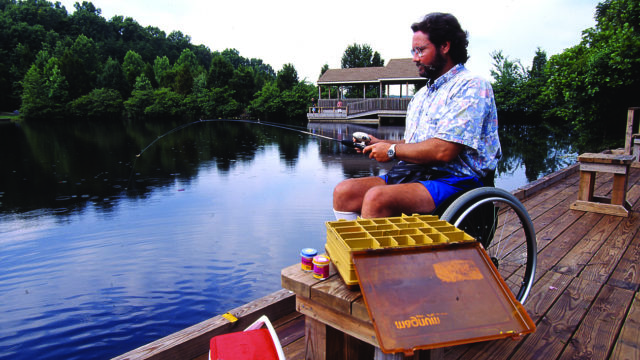 Person in a wheelchair fishing off a universally wooden accessible pier.